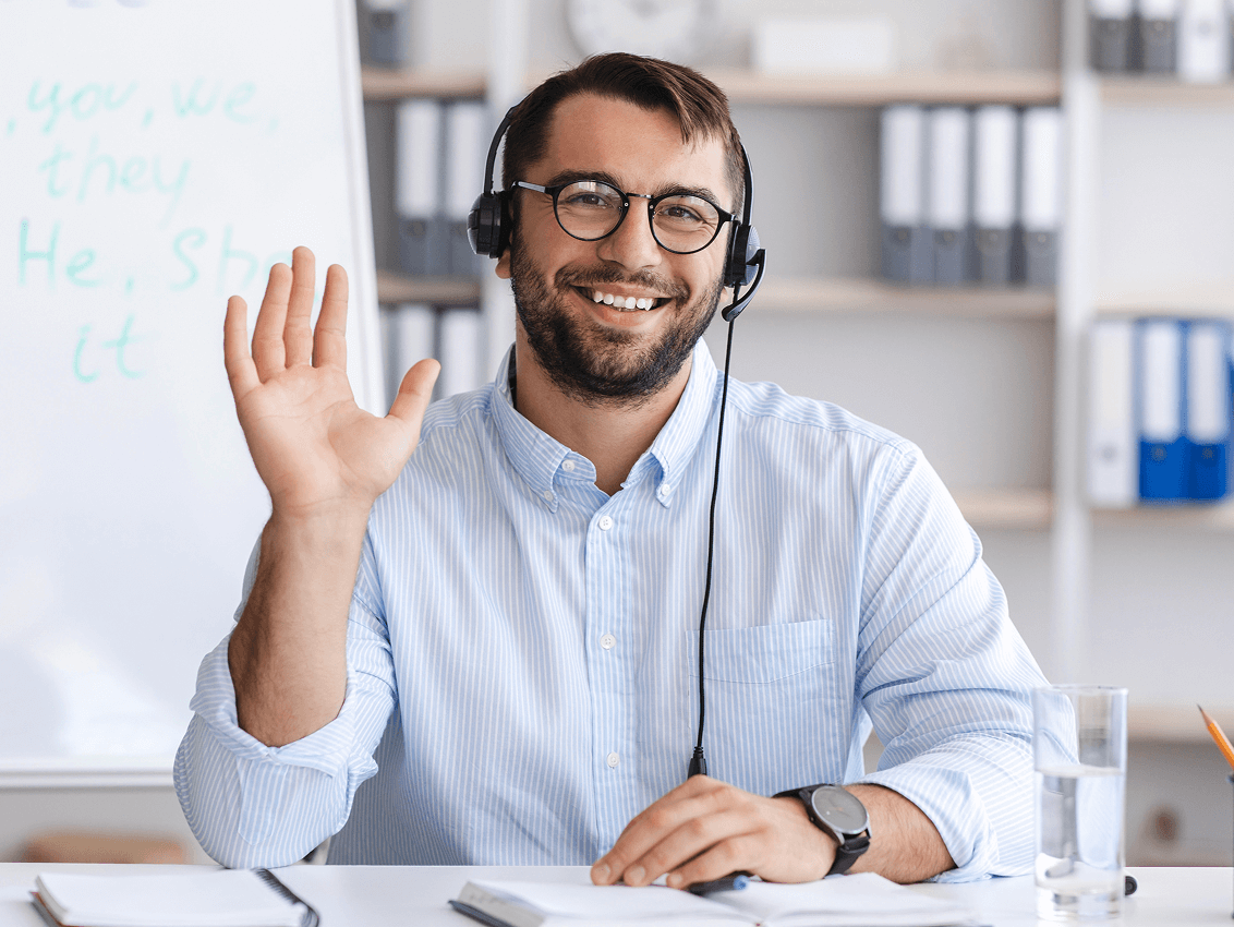 A cheerful man in a headset waves at the camera, showcasing a friendly and approachable expression.