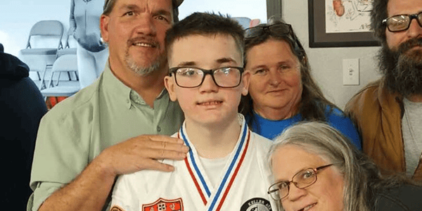 A family stands together, smiling for a photo, with a young boy in the center, capturing a moment of joy and togetherness.