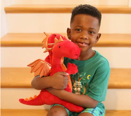 A woman and child sit at a table, smiling at each other while holding paper. Colorful children's drawings are displayed on the wall behind them.