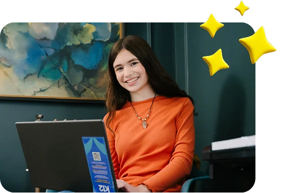 Person seated indoors using a K12 laptop, with decorative yellow star graphics in the upper corner. A framed artwork hangs on the wall in the background.