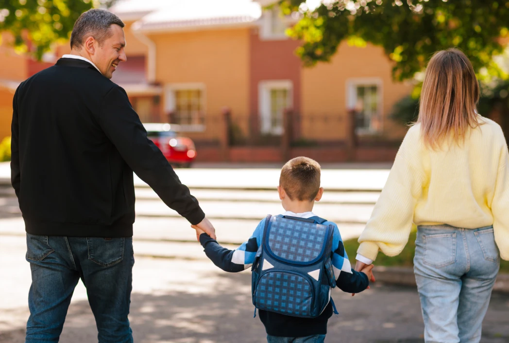 Family walking with a backpack-wearing student in a neighborhood setting, illustrating a school transition or change in school district.