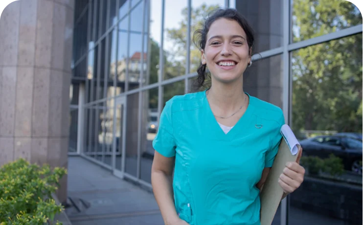 Health sciences student or professional holding a clipboard outside a healthcare facility, representing career pathways in health and human services.