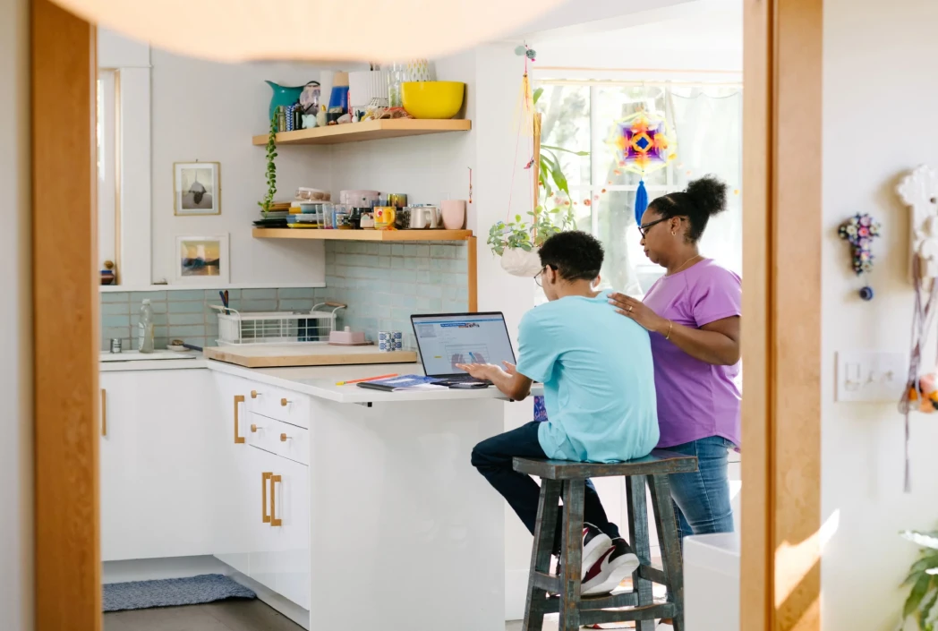 Learner participating in online school at home while receiving support during a family morning routine, highlighting structure, encouragement, and academic success.