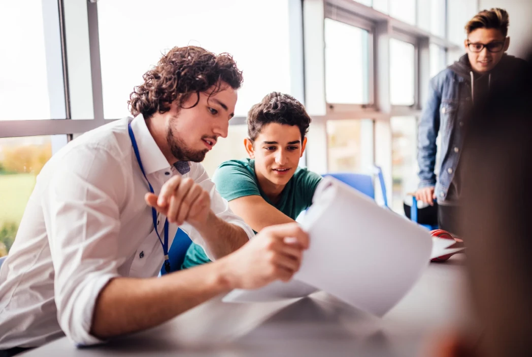 Teacher supporting students during a hybrid learning activity, combining in-person instruction, collaboration, and personalized academic guidance.